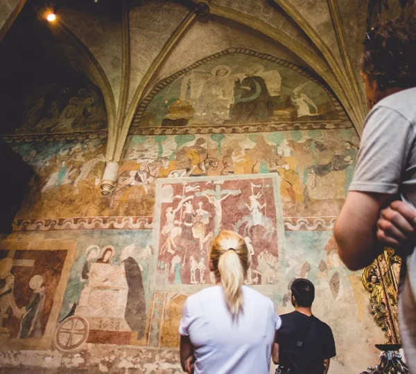 A group of people are looking at rare medieval frescoes in Church of the Holy Spirit in Žehra. UNESCO site.